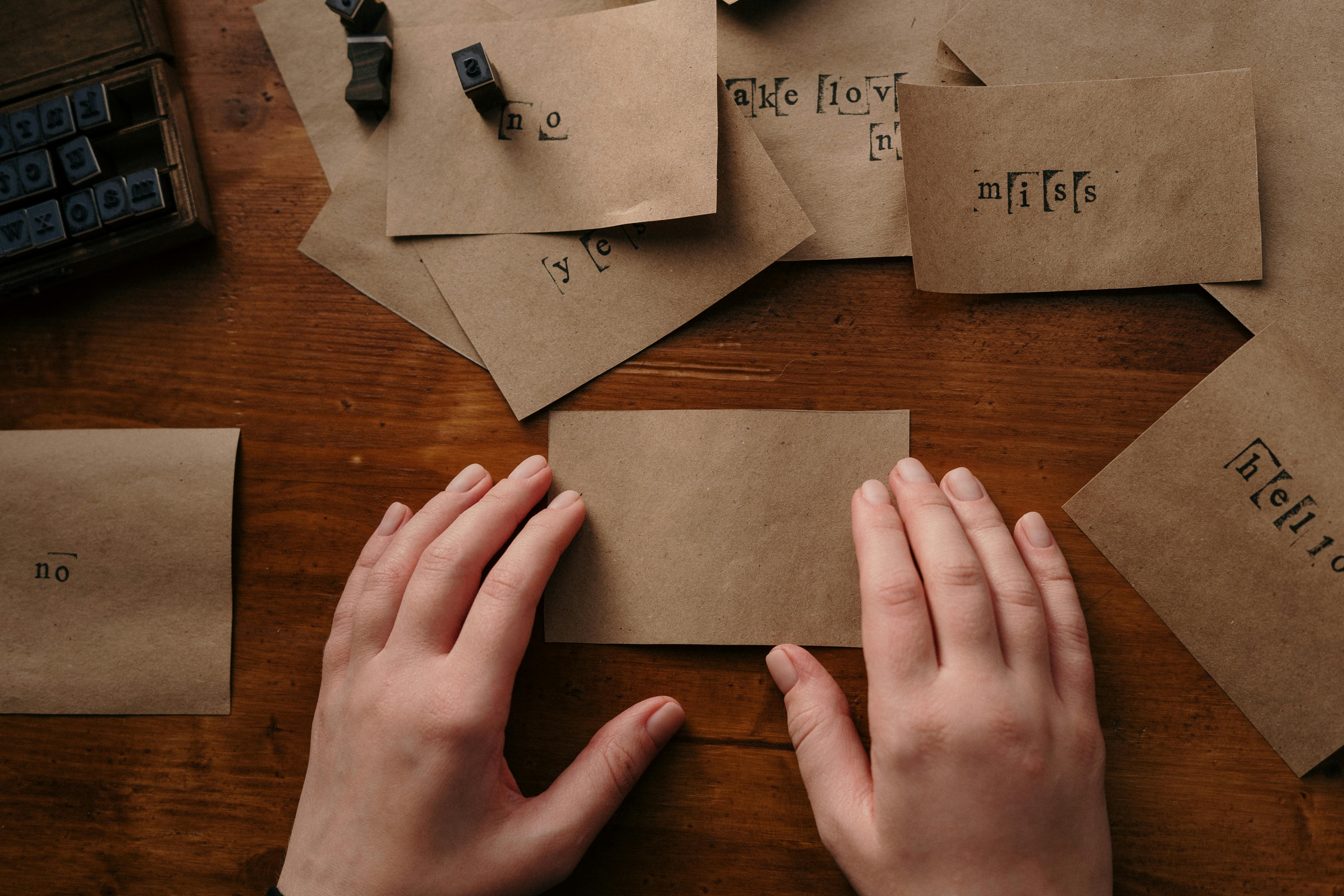 Hands arranging vintage papers with wooden alphabet stamps on a wooden table.