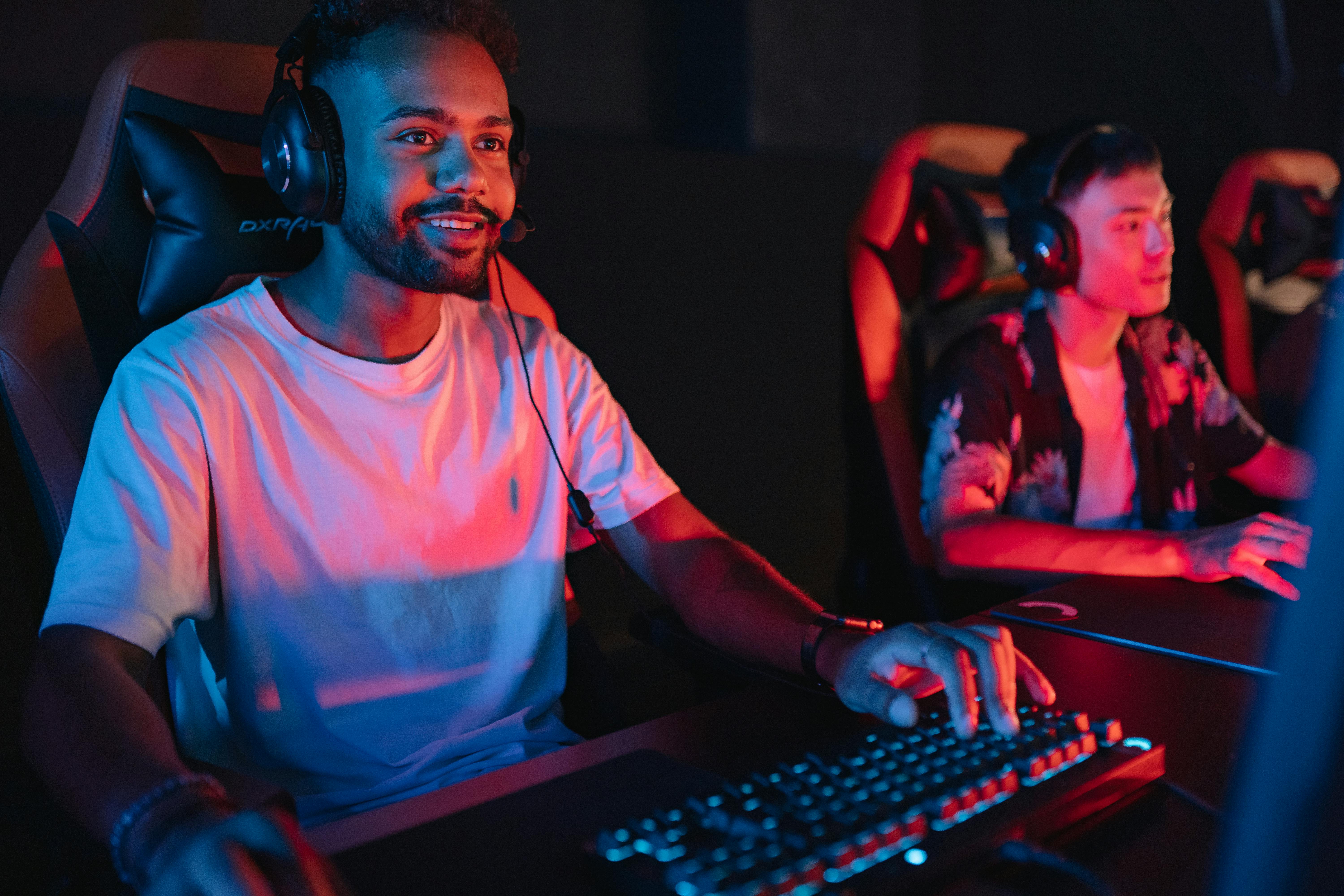 Two male gamers intensely focused during a gaming session in a cybercafe with colorful lighting.